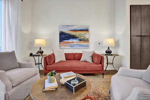 A living room with a red couch and a painting on the wall.
